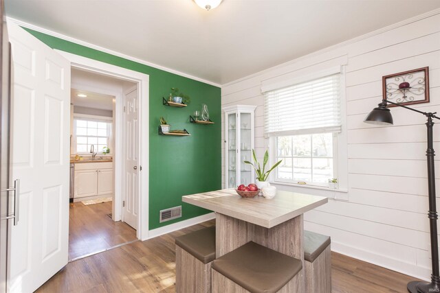 dining area with crown molding, wood walls, baseboards, dark wood-type flooring, and visible vents