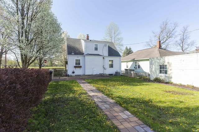 rear view of house featuring fence, a chimney, a yard, and a shingled roof