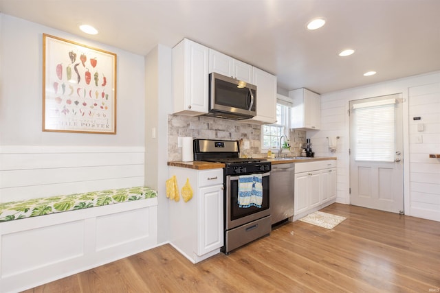 kitchen with appliances with stainless steel finishes, a sink, light wood-style flooring, white cabinetry, and decorative backsplash