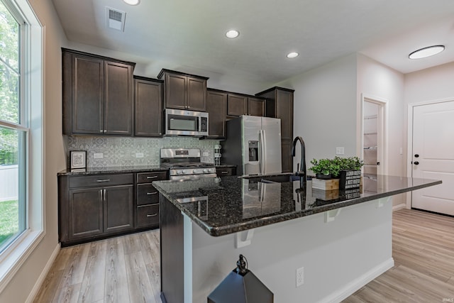 kitchen featuring dark brown cabinets, appliances with stainless steel finishes, light wood-style floors, a kitchen breakfast bar, and visible vents
