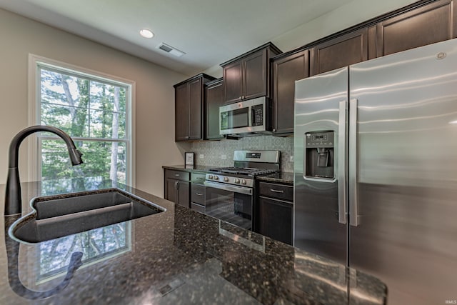 kitchen with dark brown cabinetry, visible vents, a sink, dark stone countertops, and stainless steel appliances