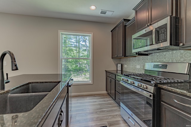 kitchen featuring visible vents, dark brown cabinets, a sink, dark stone counters, and stainless steel appliances