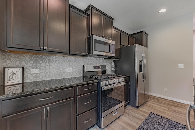 kitchen with dark brown cabinetry, dark stone counters, light wood finished floors, backsplash, and stainless steel appliances