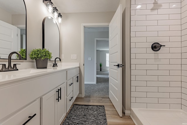 full bath with double vanity, a tile shower, a sink, and wood finished floors