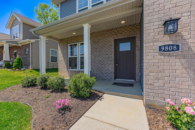 doorway to property with a porch and brick siding