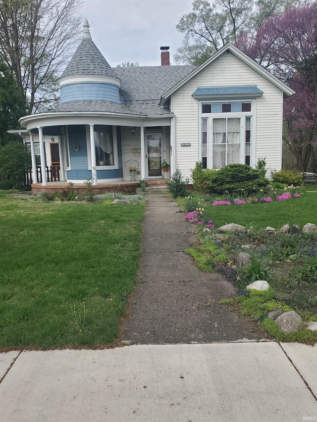victorian house featuring covered porch, a chimney, and a front yard