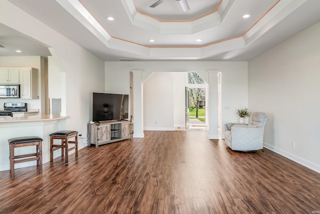 living room with ceiling fan, baseboards, dark wood-style floors, ornamental molding, and a tray ceiling