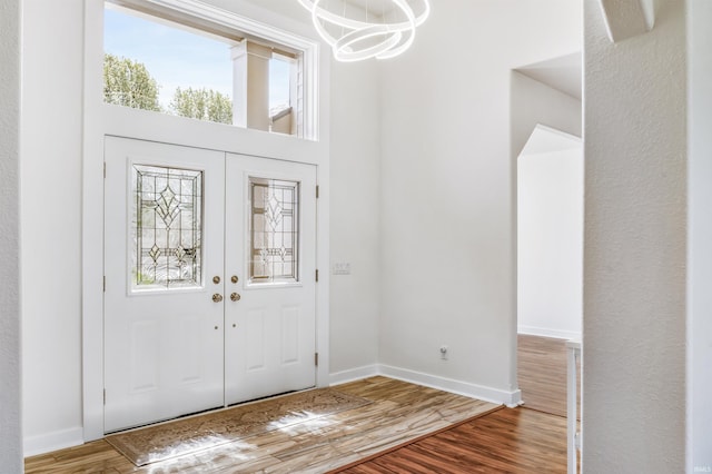 foyer with an inviting chandelier, baseboards, wood finished floors, and french doors
