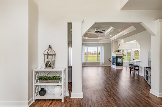 living room featuring ceiling fan, a raised ceiling, a multi sided fireplace, baseboards, and wood finished floors
