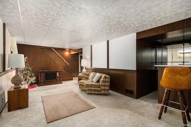 carpeted living room featuring wooden walls, a drop ceiling, and visible vents