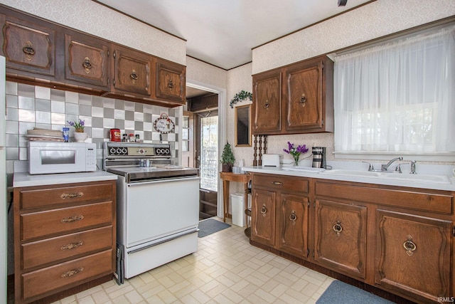 kitchen with a sink, backsplash, white appliances, and light countertops