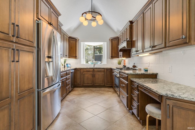 kitchen with under cabinet range hood, light stone counters, appliances with stainless steel finishes, backsplash, and vaulted ceiling