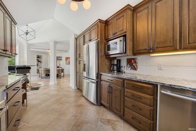 kitchen with light stone countertops, appliances with stainless steel finishes, decorative columns, tasteful backsplash, and vaulted ceiling
