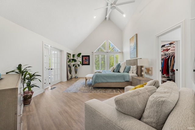 bedroom featuring light wood finished floors, a walk in closet, multiple windows, and high vaulted ceiling