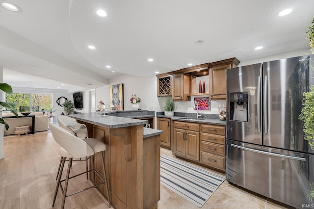 kitchen with a breakfast bar area, brown cabinetry, a sink, stainless steel fridge with ice dispenser, and a peninsula