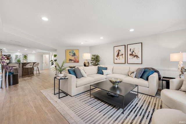 living area with a wainscoted wall, light wood finished floors, indoor bar, and recessed lighting