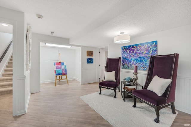 sitting room with wainscoting, light wood finished floors, a textured ceiling, stairs, and visible vents