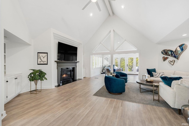 living area with ceiling fan, high vaulted ceiling, a glass covered fireplace, light wood-style flooring, and beamed ceiling