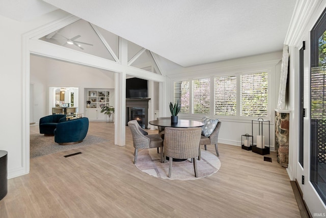dining area with baseboards, light wood-style flooring, a glass covered fireplace, and ceiling fan