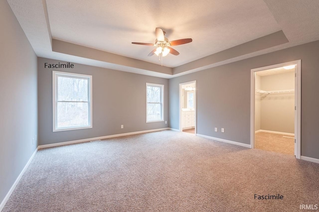 unfurnished bedroom featuring carpet flooring, baseboards, a spacious closet, and a raised ceiling