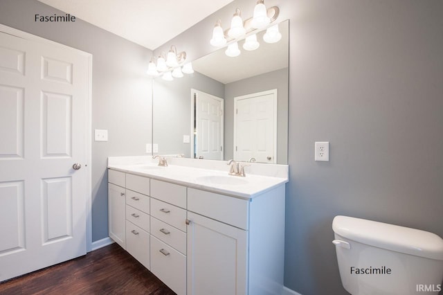 bathroom with double vanity, wood finished floors, a sink, baseboards, and toilet