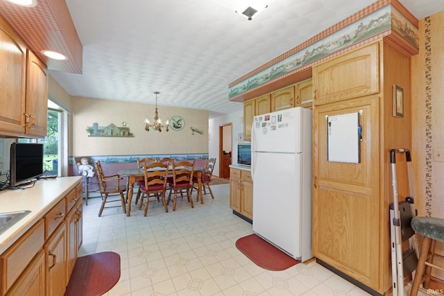kitchen featuring hanging light fixtures, light countertops, freestanding refrigerator, an inviting chandelier, and light floors