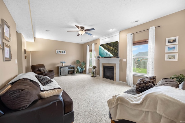 carpeted living room with ceiling fan, a textured ceiling, visible vents, a fireplace with flush hearth, and baseboards