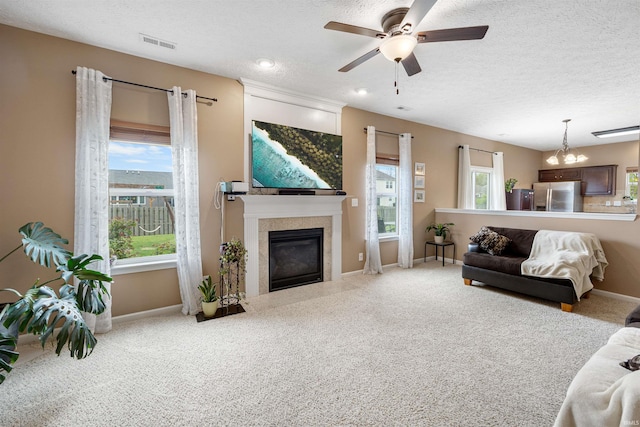 living room featuring carpet floors, a tiled fireplace, ceiling fan with notable chandelier, baseboards, and visible vents