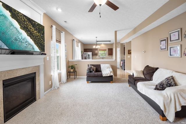 carpeted living area with a textured ceiling, a glass covered fireplace, a ceiling fan, baseboards, and visible vents