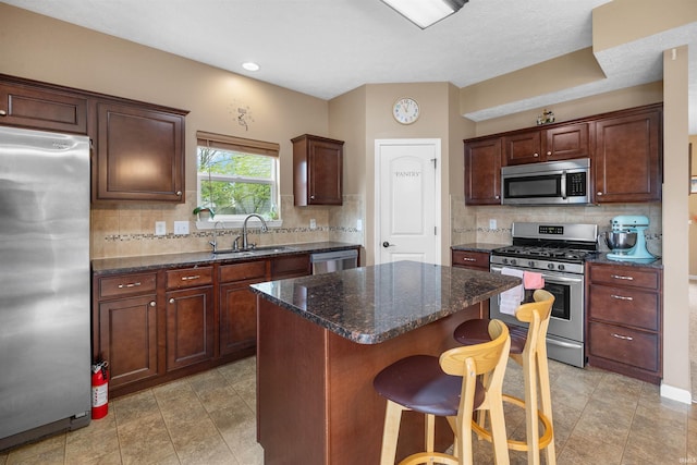 kitchen featuring a kitchen island, backsplash, a sink, a breakfast bar, and stainless steel appliances