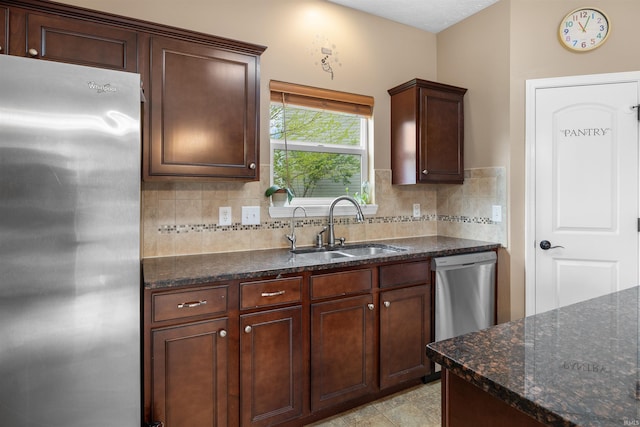 kitchen featuring a sink, tasteful backsplash, stainless steel appliances, and dark stone countertops