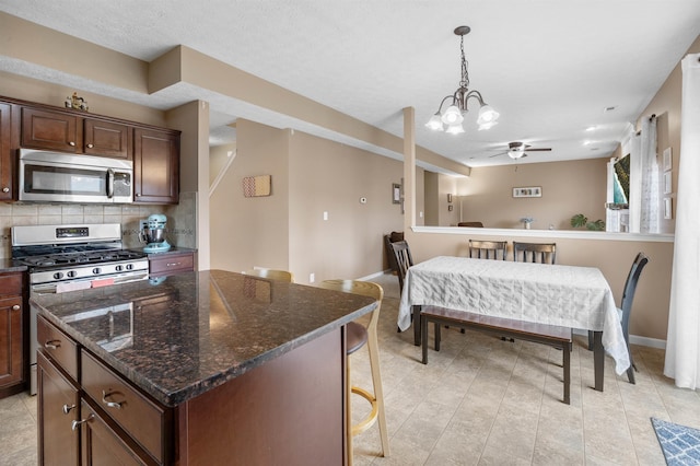 kitchen featuring decorative backsplash, pendant lighting, appliances with stainless steel finishes, a center island, and ceiling fan with notable chandelier