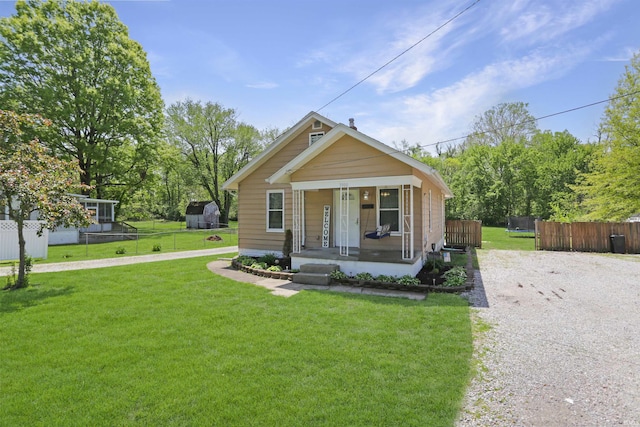 bungalow-style home with covered porch, fence, driveway, and a front lawn