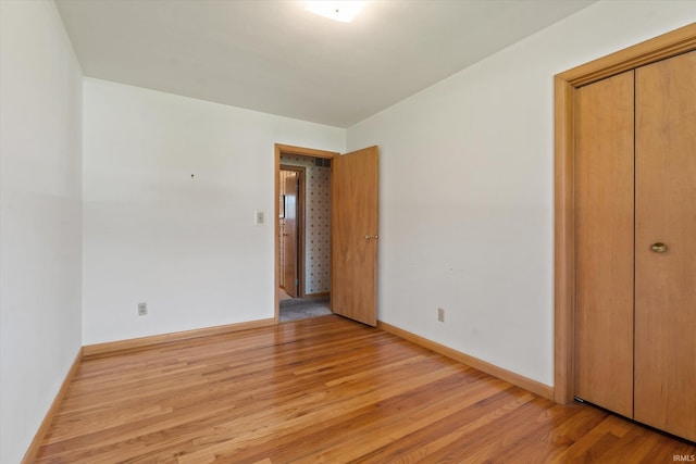 unfurnished bedroom featuring light wood-style floors, baseboards, and a closet