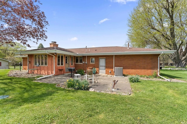 rear view of property with a patio, a chimney, brick siding, central air condition unit, and a yard