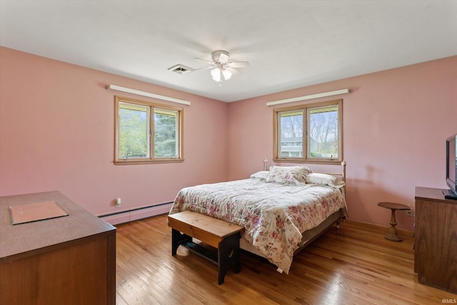 bedroom with ceiling fan, a baseboard heating unit, visible vents, and light wood-type flooring