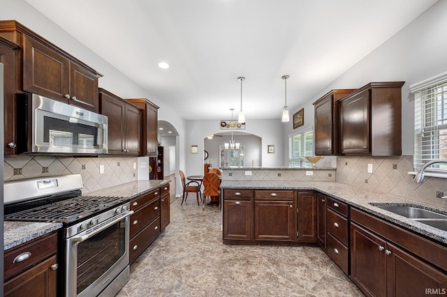 kitchen featuring light stone counters, appliances with stainless steel finishes, a sink, arched walkways, and a peninsula