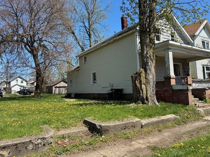 view of property exterior featuring a porch, a lawn, and a chimney