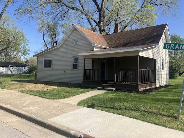 view of front of home featuring roof with shingles, covered porch, a chimney, and a front lawn
