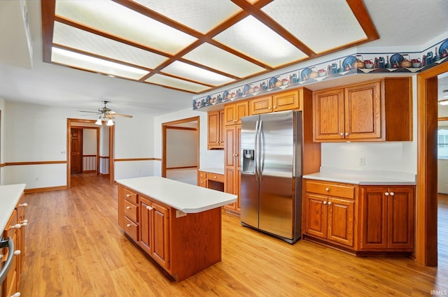 kitchen with stainless steel fridge, light countertops, a center island, brown cabinets, and light wood-style flooring