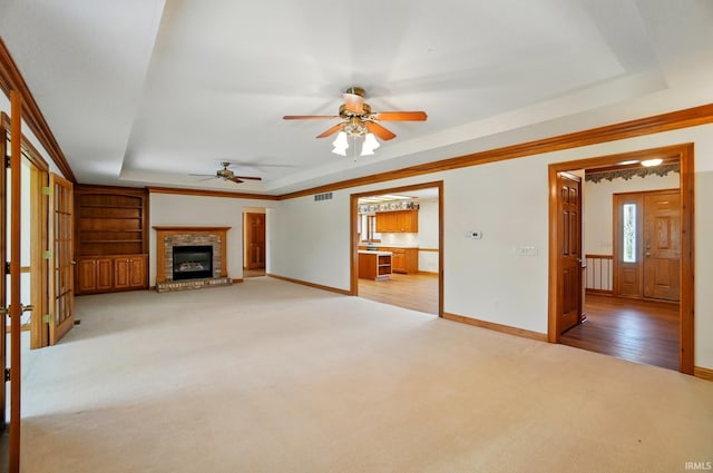 unfurnished living room with a ceiling fan, visible vents, a raised ceiling, baseboards, and light carpet