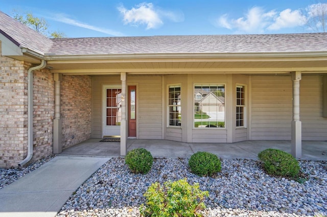 property entrance with brick siding, roof with shingles, and a porch