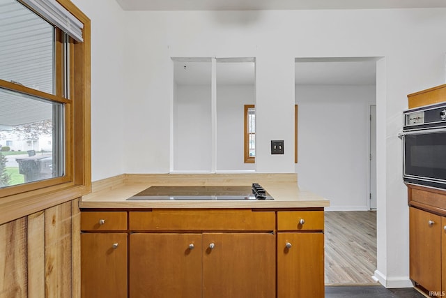 kitchen featuring light countertops, brown cabinetry, black appliances, and dark wood-type flooring
