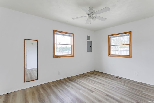 unfurnished room with a healthy amount of sunlight, electric panel, a ceiling fan, and light wood finished floors