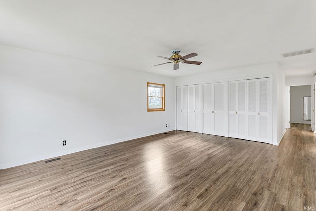 unfurnished bedroom with two closets, visible vents, and wood finished floors