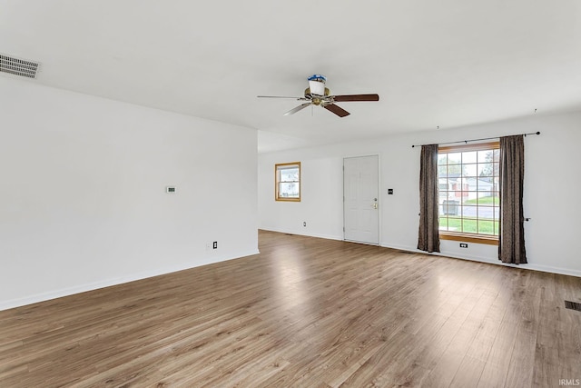 empty room featuring a ceiling fan, baseboards, visible vents, and wood finished floors