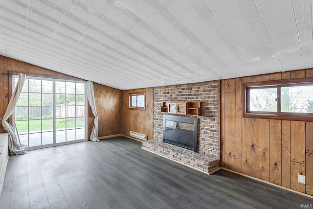 unfurnished living room with wood walls, a baseboard heating unit, a wealth of natural light, and a fireplace