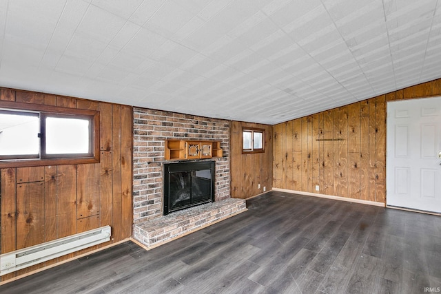 unfurnished living room featuring plenty of natural light, a baseboard heating unit, wooden walls, and a fireplace