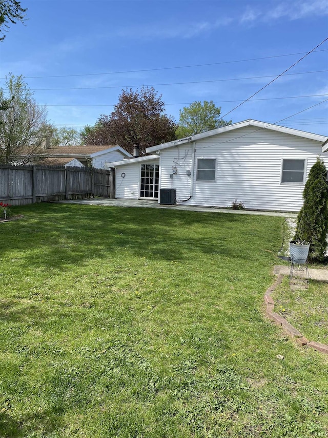 rear view of house with fence, a lawn, and central AC