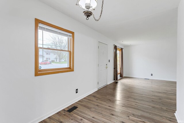 spare room with baseboards, a notable chandelier, wood finished floors, and visible vents